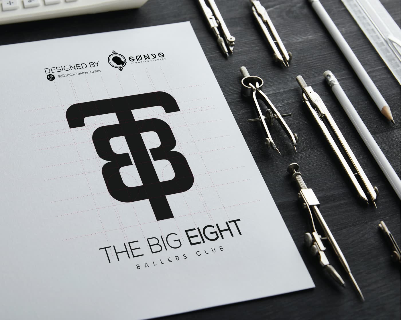A black monogram on a white sheet beside drawing instruments