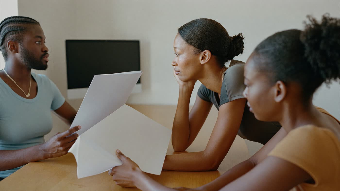 A facilitator standing at a table teaching a small team of professionals in a daylit office